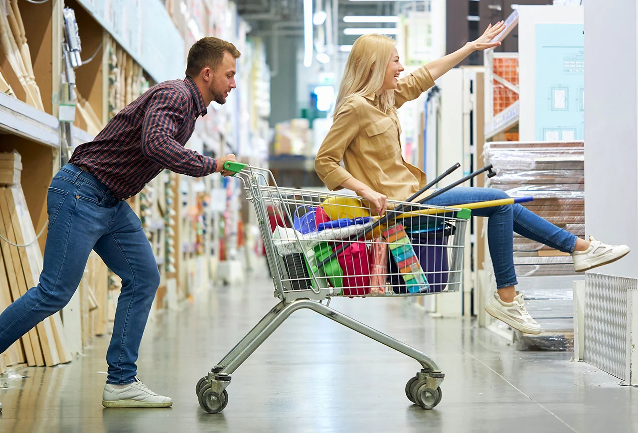 young caucasian married couple enjoy shopping together, woman riding a trolley in hypermarket, happy shopaholics concept